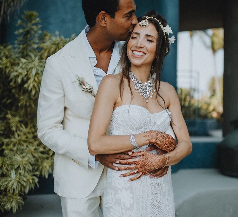 Bride in cream suit embraces bride in boho lace wedding dress and traditional matha patti at Tigre Del Mar wedding