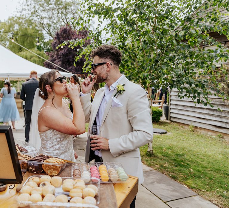 The bride and groom help themselves to cookies and macarons at their outdoor wedding drinks 