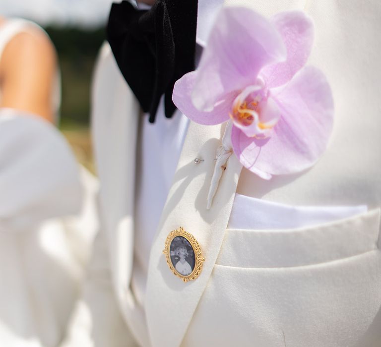 Groom wearing white suit with a orchid buttonhole and personalised pin