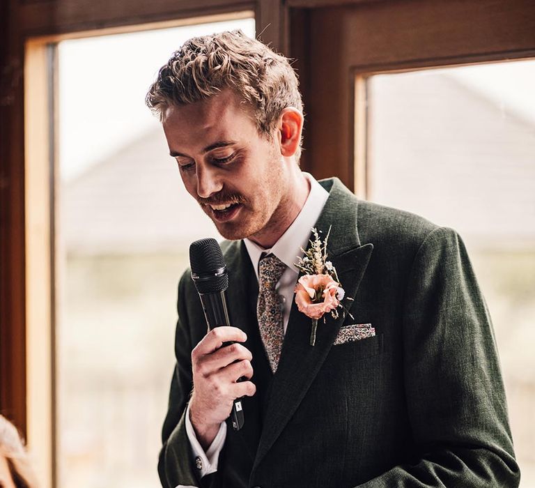 Groom in a dark green wedding suit reading out his wedding speech 