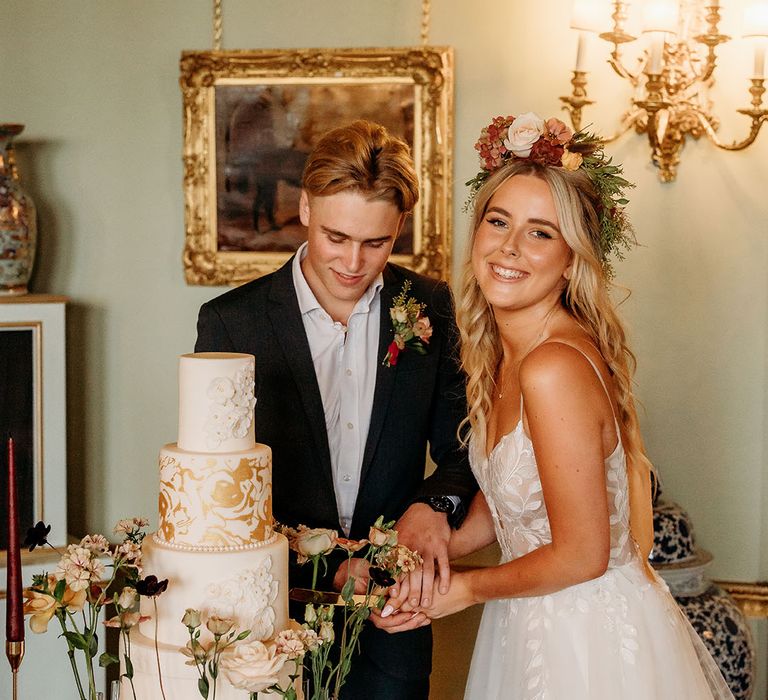 The bride and groom cut their white and gold wedding cake for autumn wedding theme 