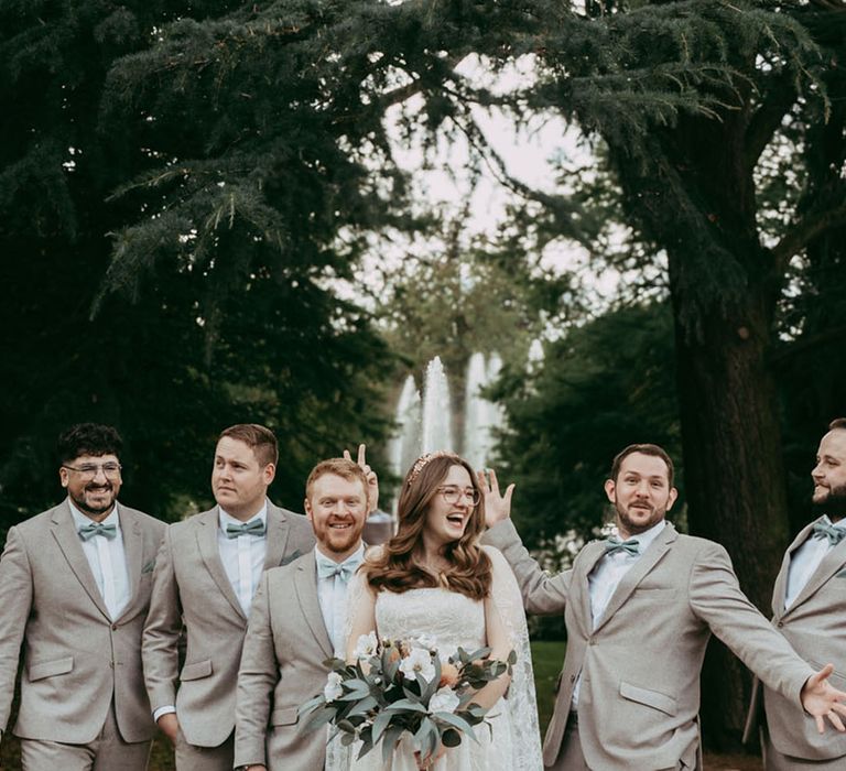 Bride and groom pose with the groomsmen in grey and green wedding suits 