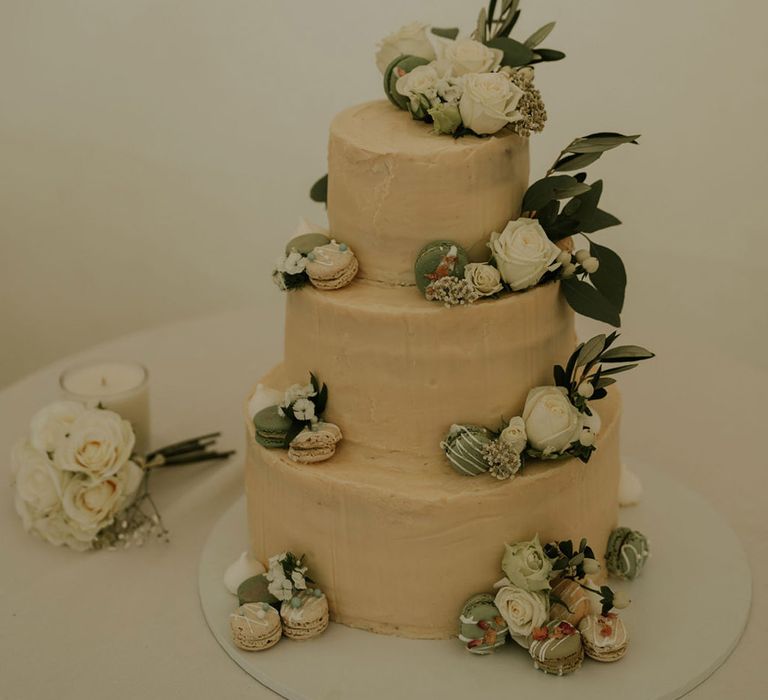 Three tier simple wedding cake decorated with white roses and green and white macarons 