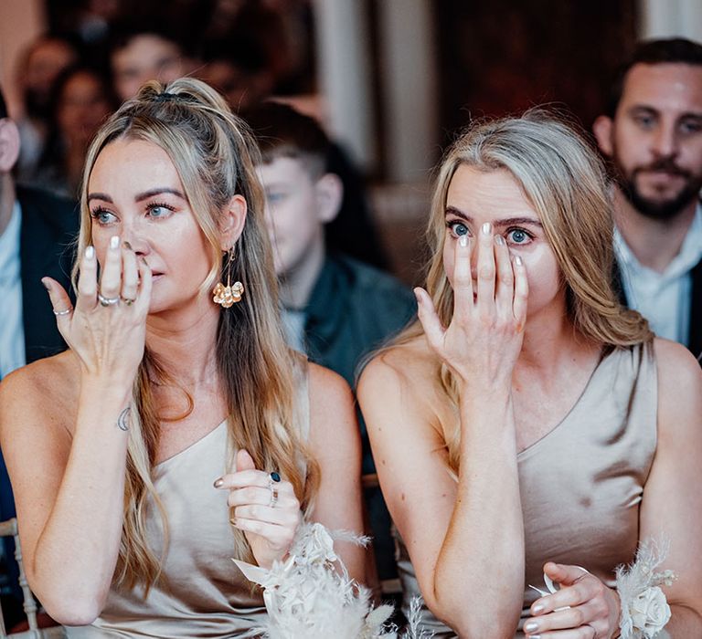 The bridesmaids in champagne gold bridesmaid dresses wipe their tears as the listen to the wedding ceremony 