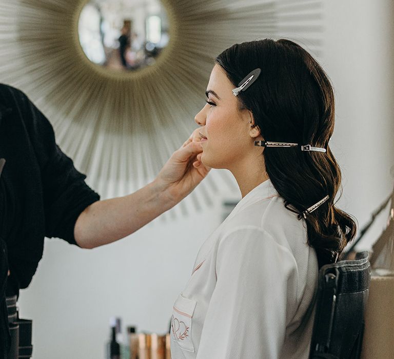 Bride in white robe getting ready for the wedding day with crocodile clips in her hair to set the Hollywood waves 