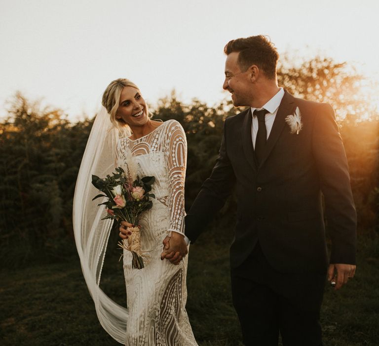 Bride and groom holding hands during sunset 