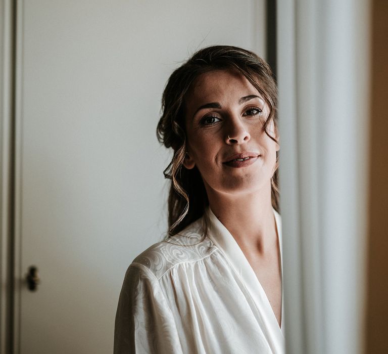 Bride with half up half down hair on the morning of the wedding in a white getting ready robe 