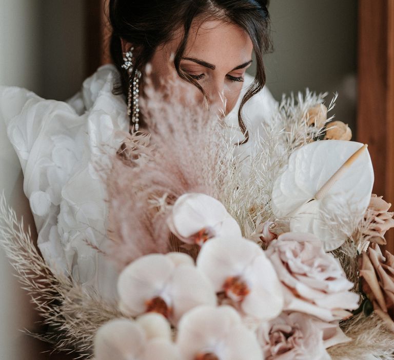 Bride holding her orchid wedding bouquet with anthuriums and dried grasses 