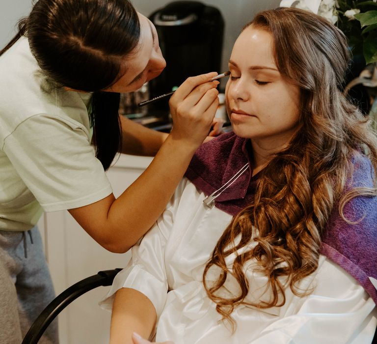 Bride with long curly brown hair having her makeup done on the wedding morning 