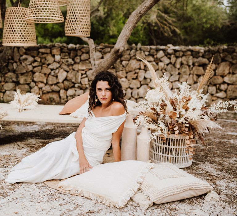 Bride sits outside with wicker lampshades and white pillows