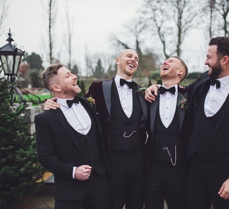 Groomsmen laughing in black and burgundy tuxedos and bow ties 