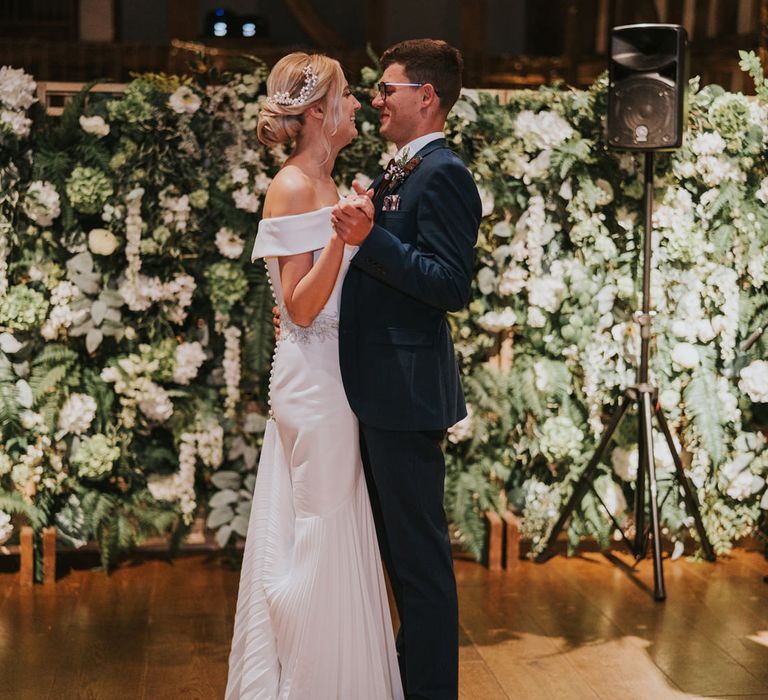 Bride & groom during their first dance with floral wall in the background