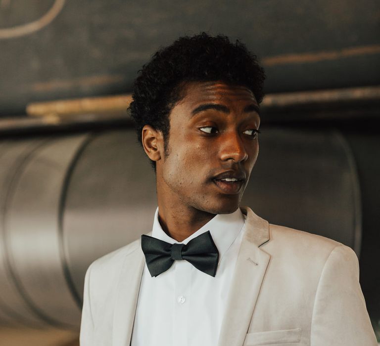 Stylish groom in a tuxedo with white shirt, black braces and bow tie, and a grey jacket 