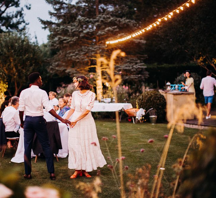 Bride and groom holding hands at their intimate garden reception with festoon light decor 