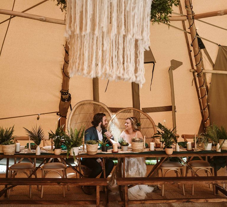 Macrame chandelier hangs from tipi with bride & groom sat at head table