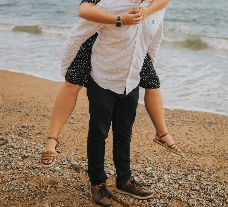 Husband to be giving his finance a piggy back on the beach for engagement photoshoot 