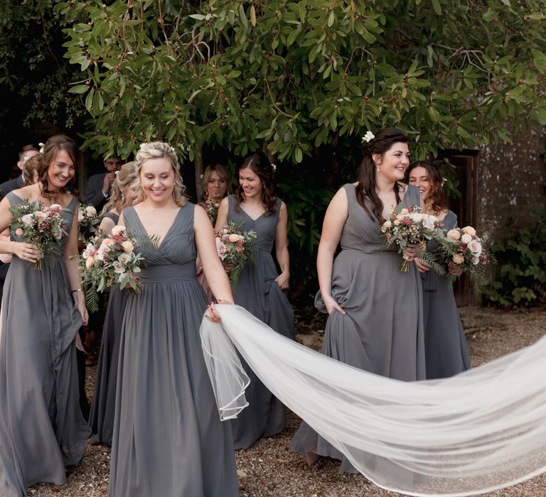 Bridesmaids holding brides sweeping veil with groomsmen in the background