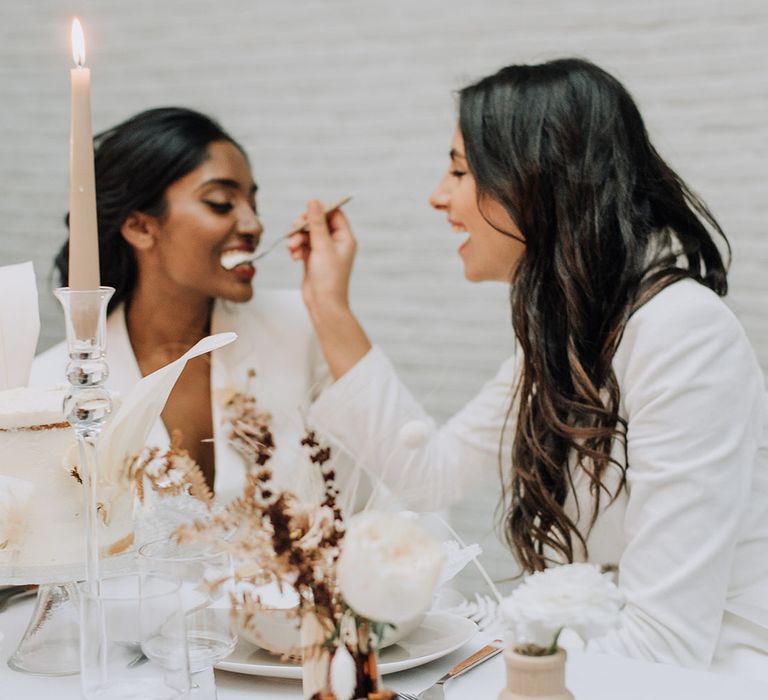 Brides feeding each other cake at all white wedding inspiration shoot