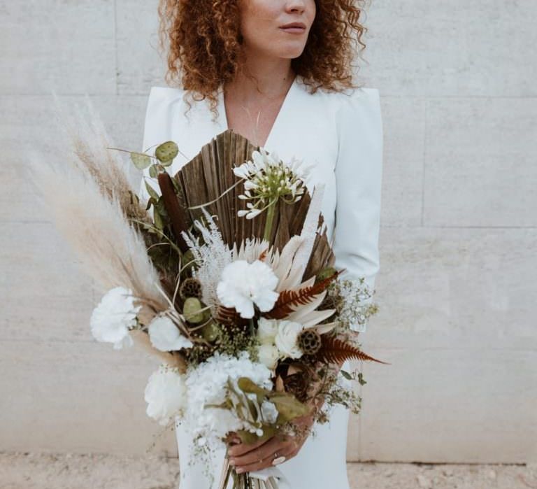 White bride with red natural curly hair holds sculptural bouquet wearing deep v neck, long sleeve minimalist wedding dress