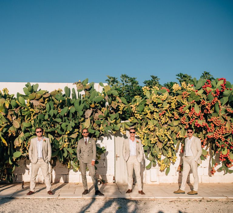 The groom and groomsmen in front of a cactus wall, wearing light coloured suits