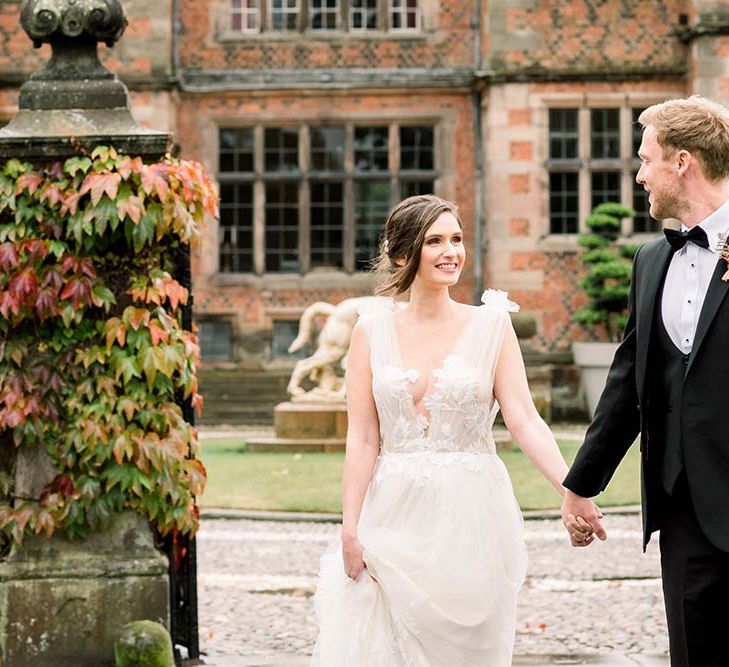 Groom in a tuxedo and horseshoe waistcoat holding his brides hand in a lace and tulle wedding dress