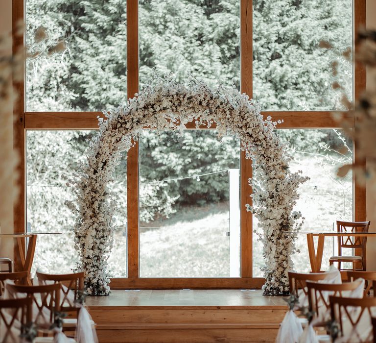 Floral archway with windows to the background and chairs lining the aisle 