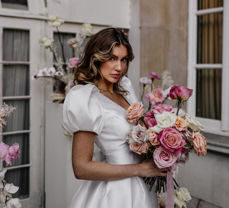 Bride holding a pink peeled rose wedding bouquet tied with ribbon 