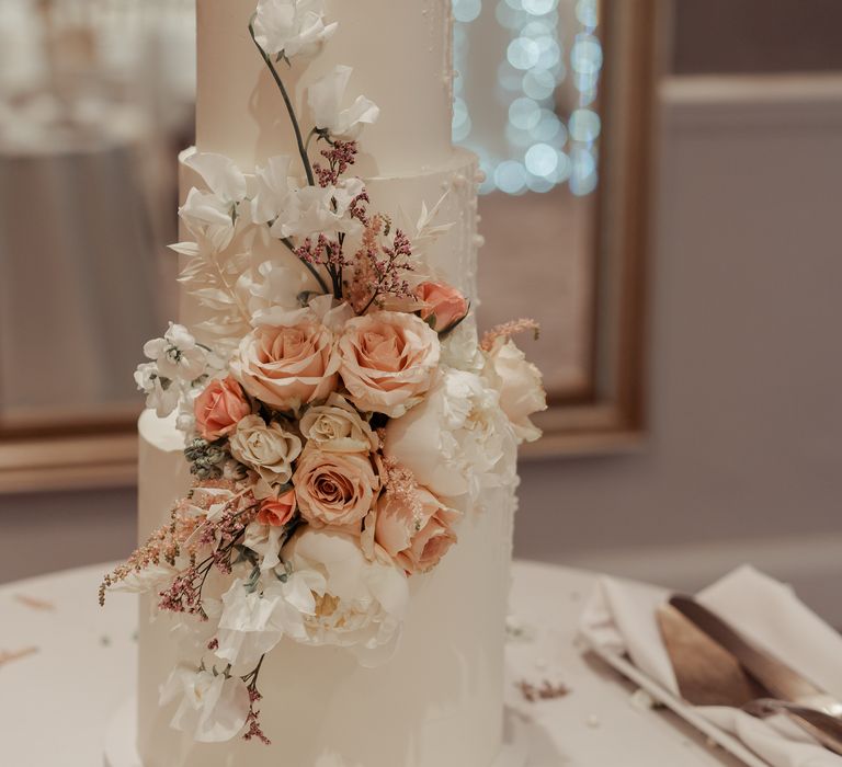 3-tier wedding cake with white frosting and floral decor with accent peach colour