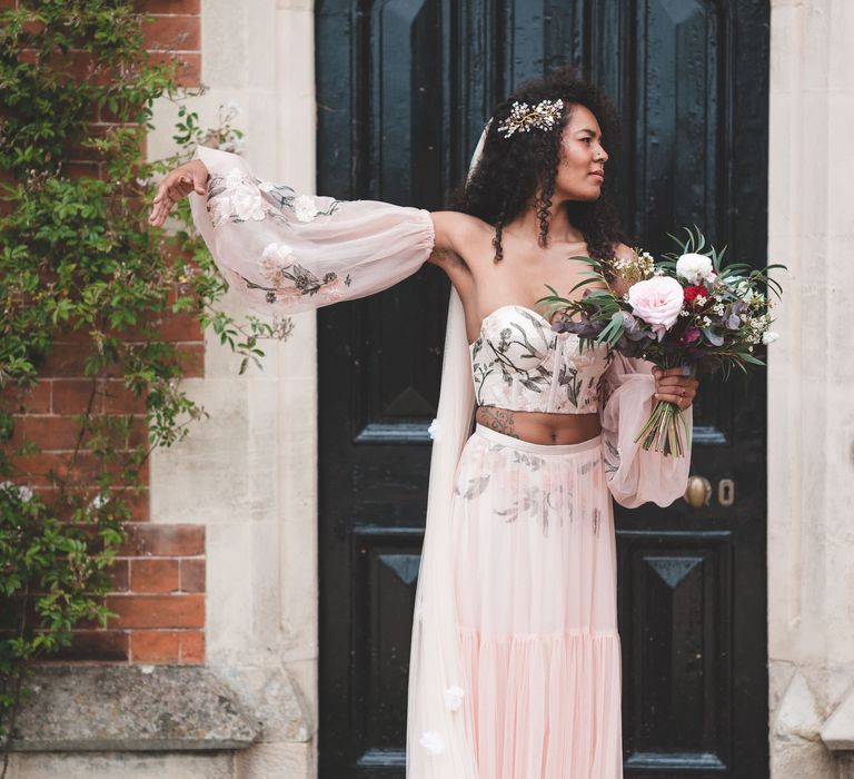 Black bride with long naturally curly hair in a blush pink with embroidery detail bridal three-piece including bodice, skirt and blouson sleeves 