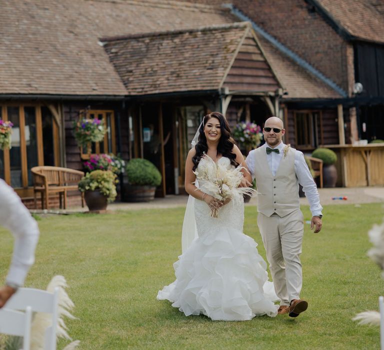 Bride in a fishtail strapless wedding dress walking down the aisle at outdoor wedding ceremony at Cooling Castle Barn