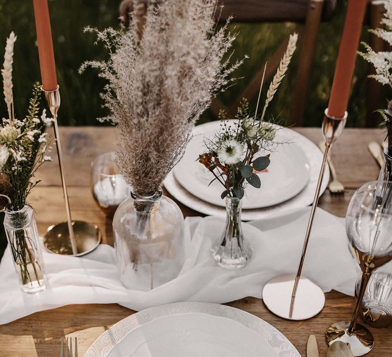 Place setting with gold cutlery and lollipop wedding favour, plus dried flower stems in vases 