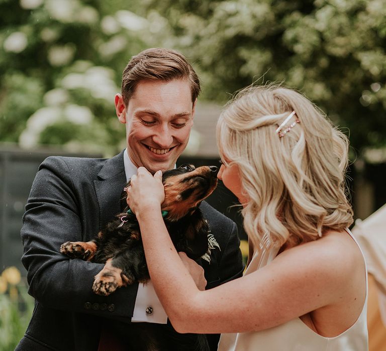 Bride and groom fussing their pet Dachshund at their DIY garden party wedding 