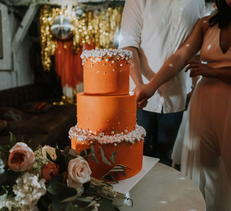 Bride and groom cutting their orange three-tier wedding cake with white ball decor 