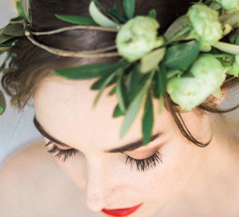 Beautiful bride in a green laurel flower crown with red lipstick, brown eyeshadow and black mascara wedding makeup 