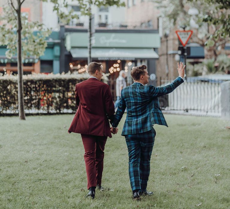 Grooms walk across grass whilst waving to people on their wedding day | Kim Williams Weddings