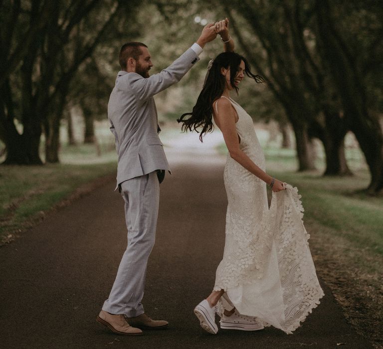 Bride in trainers dances in the grounds of country house with groom