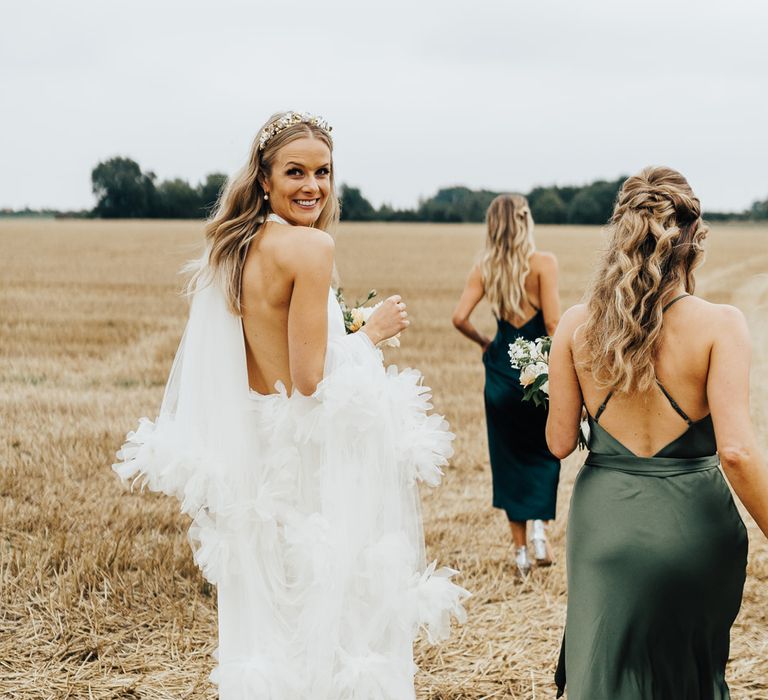 Bride in halterneck Halfpenny London wedding dress with ruffle veil and Jimmy Choo wedding shoes walks with bridesmaids in green satin bridesmaid dresses 