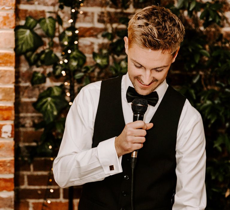 Groom in a black waistcoat and bow tie giving a speech during the wedding reception at Northbrook Park 