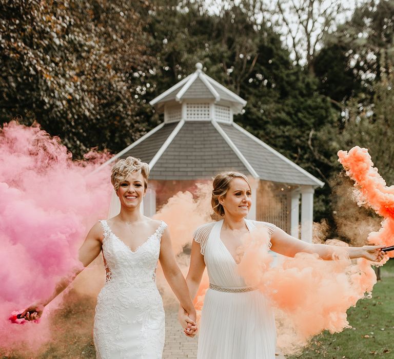 Brides hold orange and pink smoke bombs outdoors