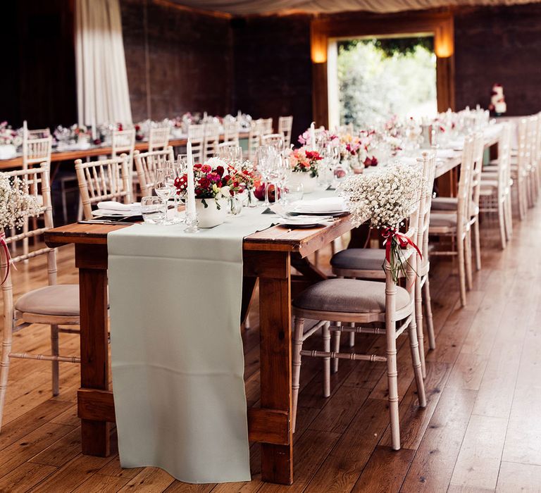 Elmore Court wedding reception room with sage green table runners, pink and red florals and white bamboo chairs