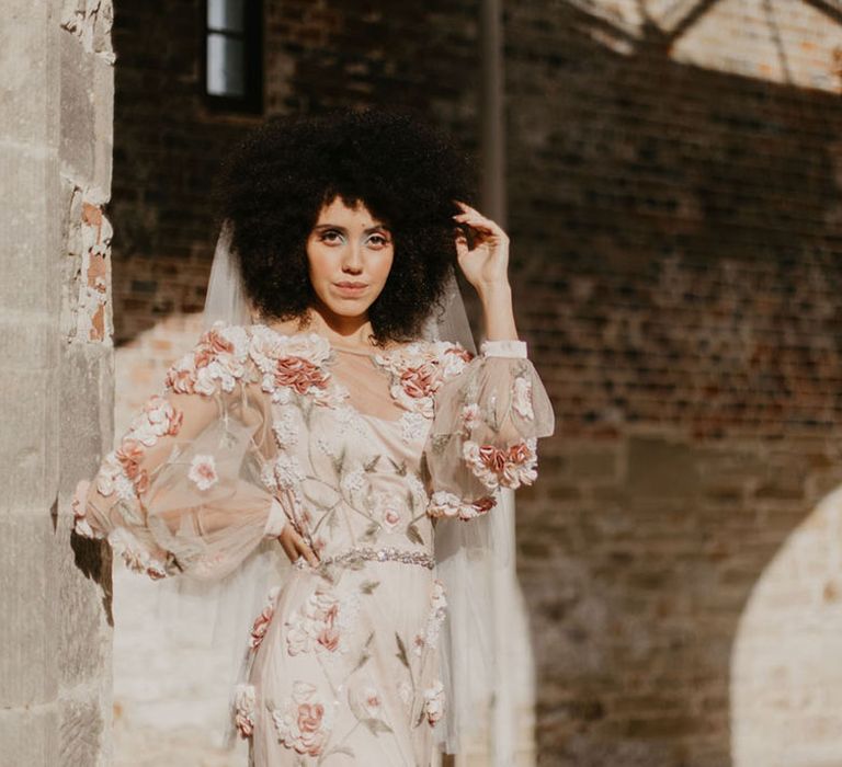 Black bride with afro hair in a 3D flower appliqué pink embroidered wedding dress with sheer long sleeves at Chiddingstone Castle wedding venue in Kent 