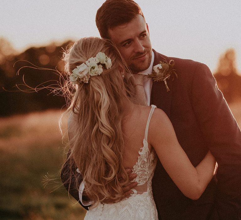 Bride in lace wedding dress with half up half down wedding hair with flowers hugs bearded groom