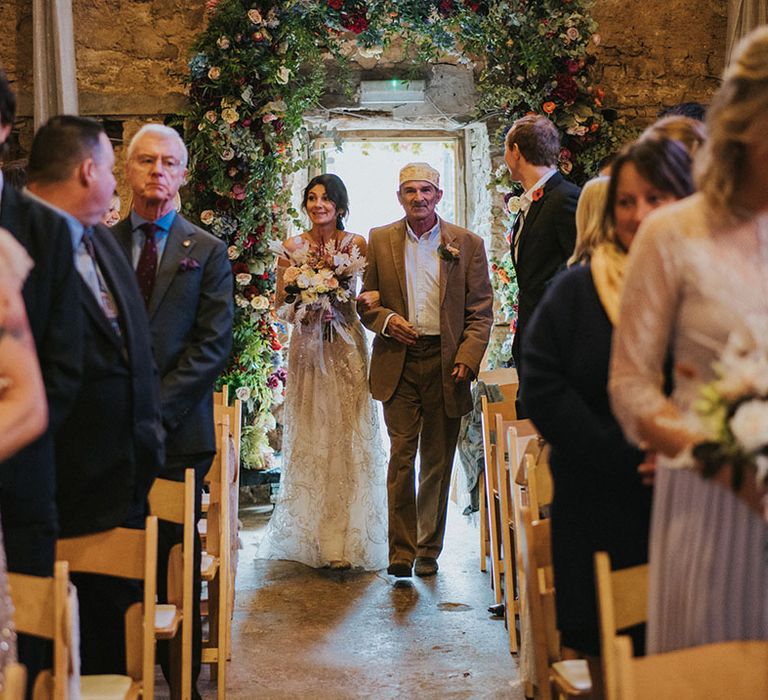 Father of the bride walks the bride down the aisle through flower archway