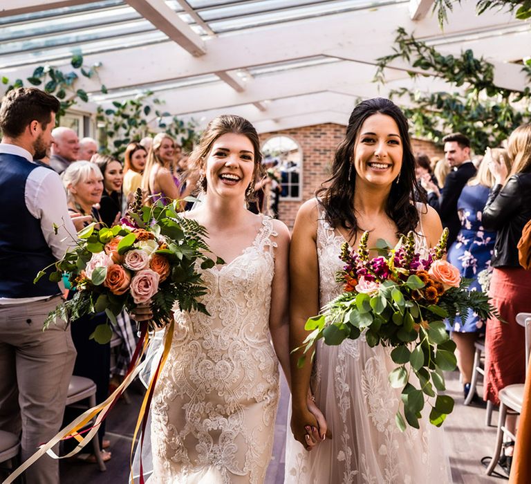 Brides in lace wedding dresses walk back down the aisle as a married couple