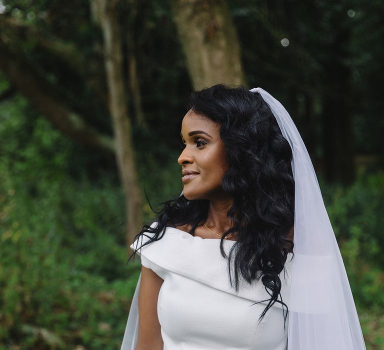 Bride with curly black hair in off the shoulder wedding dress and gold pearl necklace