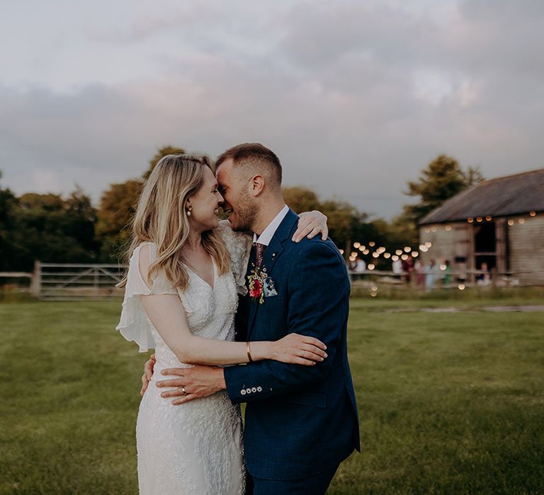 Groom in blue suit with colourful boutonnière with bride in beaded wedding dress