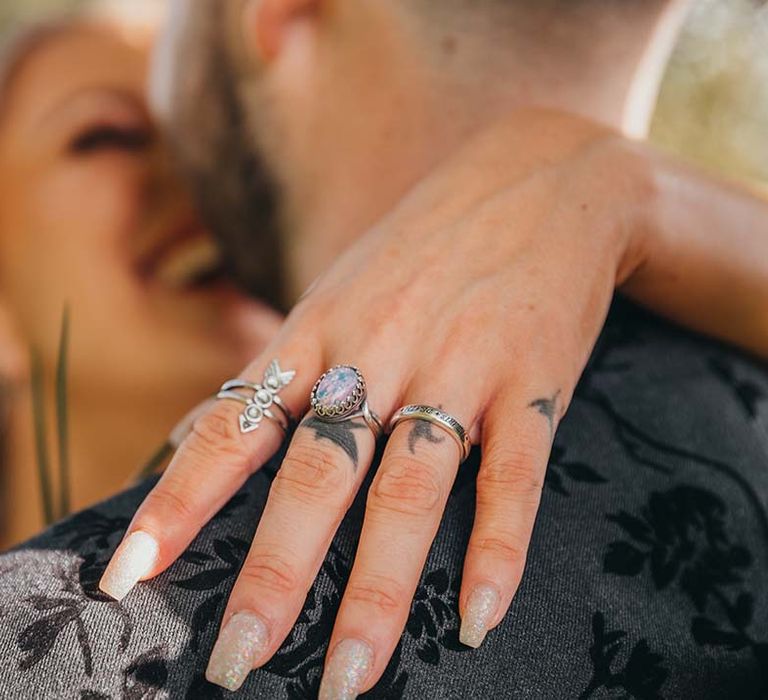 Bride and groom kiss showing bride's glittery wedding nails and silver rings on tattooed hand