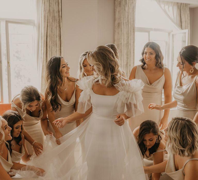 Bridesmaids in gold cowl neck satin dresses all fawn over the bride in her stunning ruffle wedding dress 