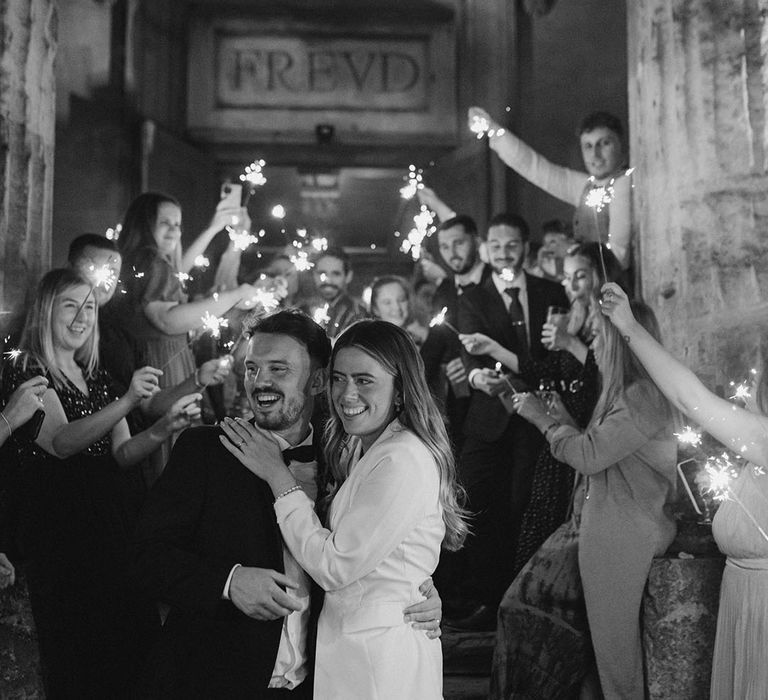 Groom in black tie smiles as he holds bride in outfit change of white blazer with white Loeffler Randall wedding shoes 