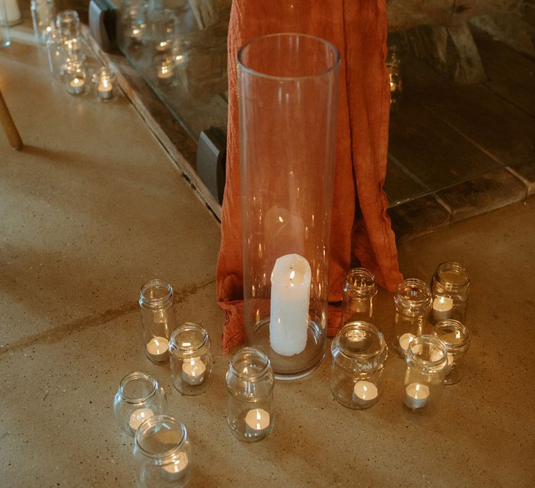 Orange wedding drapes on wooden tables with glass candleholders full of tea lights and pillar candles